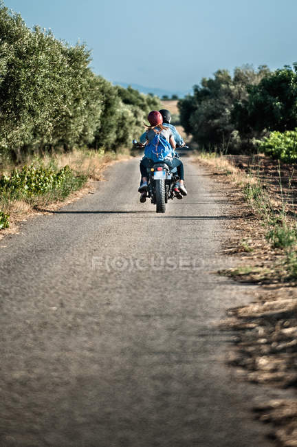Vista trasera de la pareja adulta que monta motocicleta en la carretera rural, Cagliari, Cerdeña, Italia - foto de stock