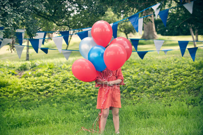 Girl holding bunch of balloons outdoors — Stock Photo