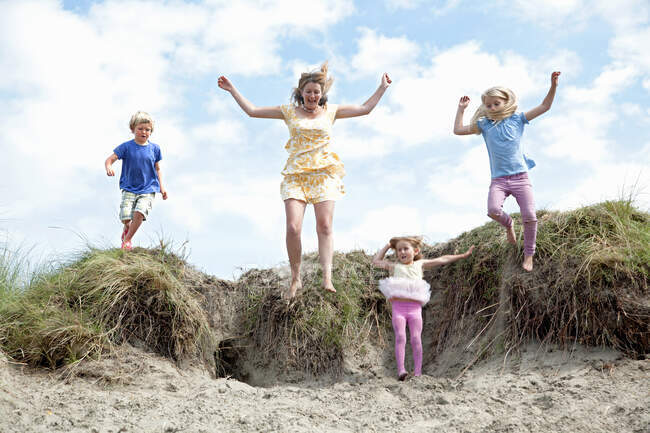 Madre con tre figli che saltano dalle dune, Galles, Regno Unito — Foto stock