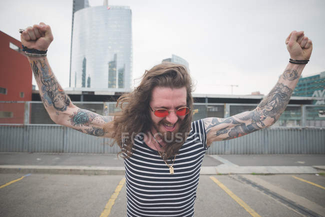 Joven hippy masculino con los brazos levantados en la azotea de la ciudad - foto de stock