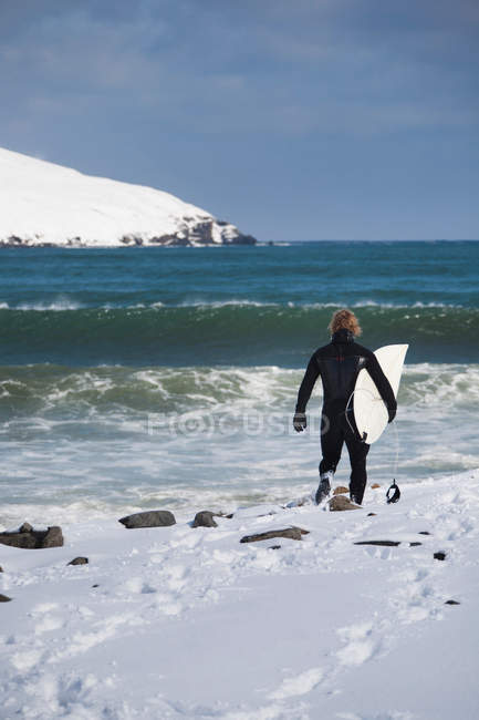 Surfer carrying surfboard on snowy beach — Stock Photo