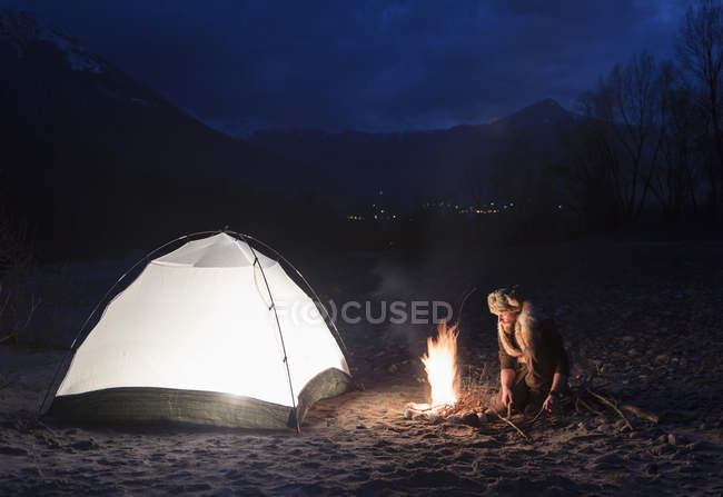 Homem pela fogueira e tenda à noite — Fotografia de Stock