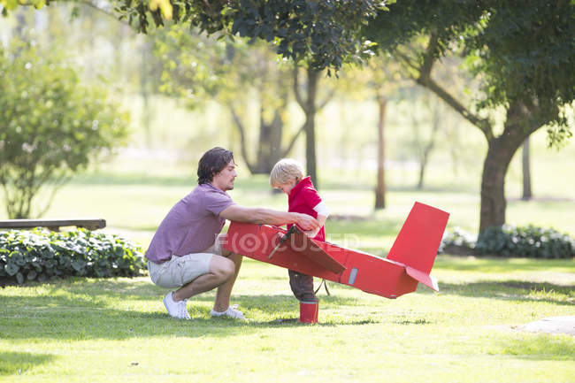 Pai agachado para preparar avião de brinquedo para filho no parque — Fotografia de Stock