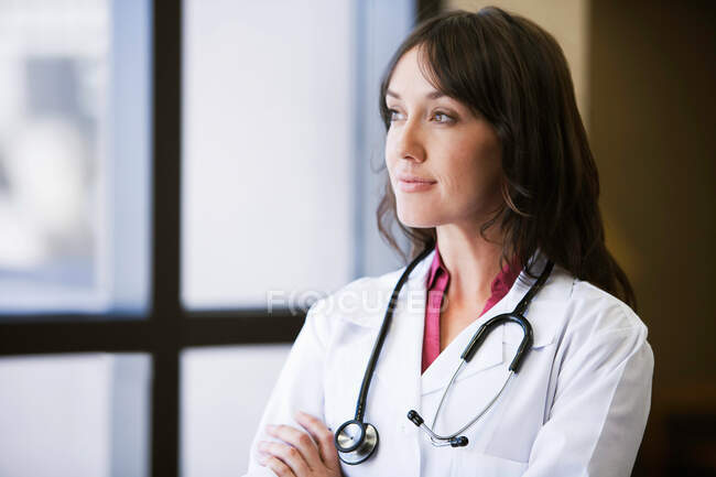 Médico femenino mirando por la ventana - foto de stock