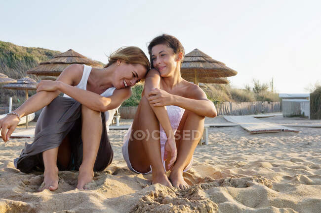Two happy women sitting on sand at beach — Stock Photo