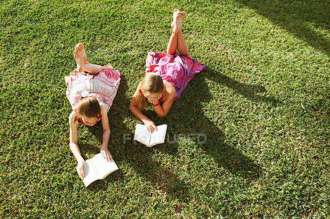 Chicas tumbadas en la hierba leyendo libros - foto de stock