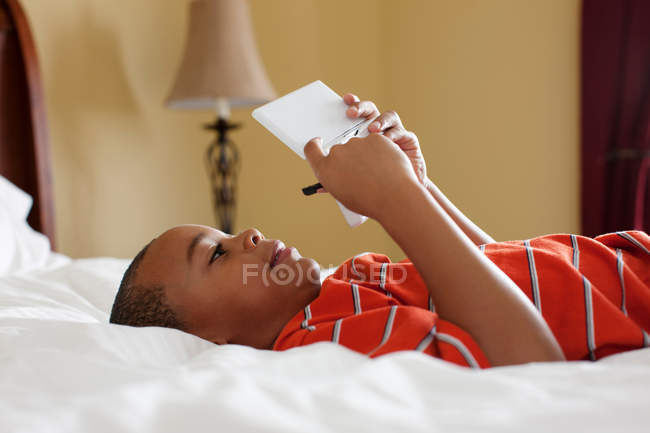 Мальчик играет в карманную видеоигру на кровати — стоковое фото