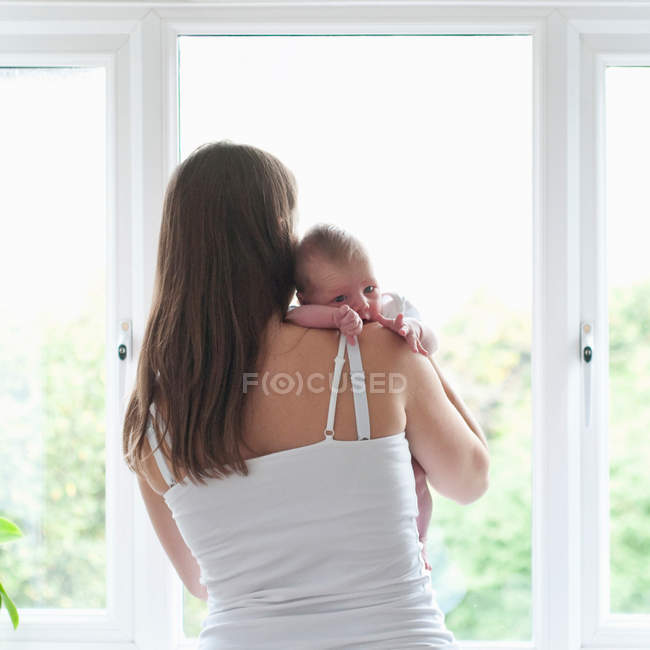 Madre sosteniendo bebé hijo por ventana - foto de stock