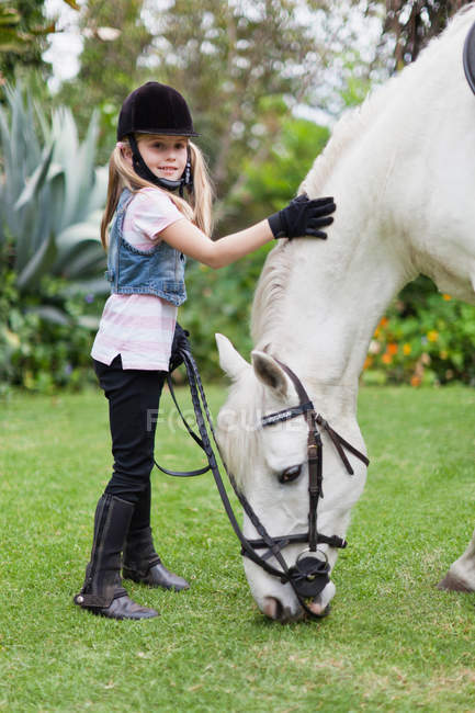 Girl petting grazing horse in park, focus on foreground — Stock Photo