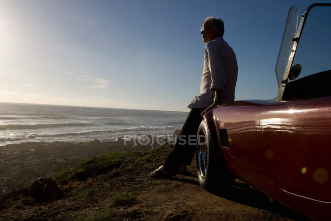 Homme plus âgé vues coucher de soleil du capot de voiture — Photo de stock