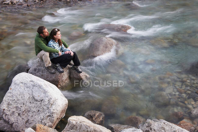 Pareja adulta sentada sobre rocas en el río - foto de stock