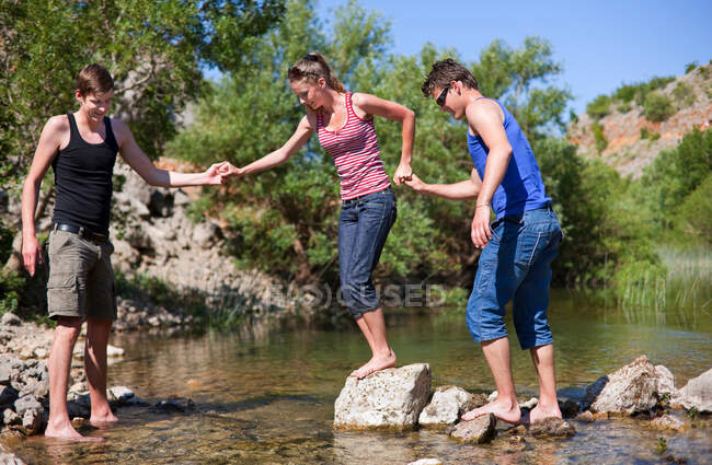 Adolescentes atravessando o rio rochoso — Fotografia de Stock