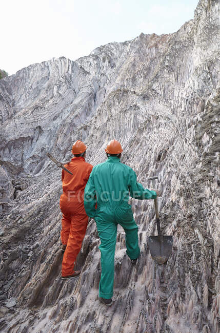 Dos trabajadores masculinos con herramientas de excavación, mina de sal exterior, vista trasera - foto de stock