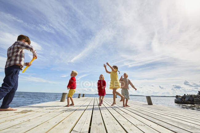 Group of young friends playing on wooden pier — Stock Photo