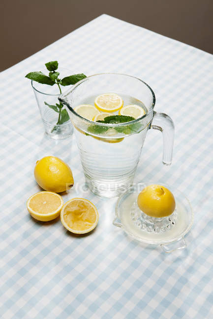 Lemons with herbs and pitcher of water — Stock Photo