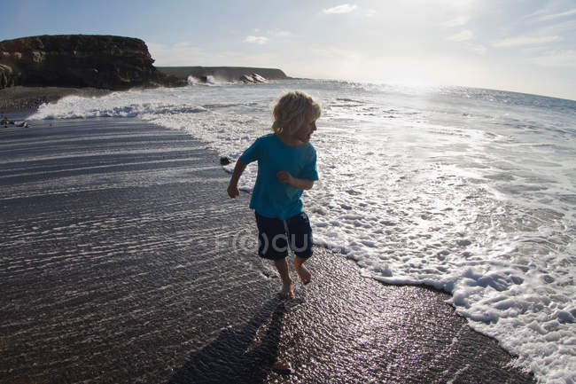 Garçon jouer dans les vagues sur la plage — Photo de stock