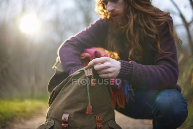 Чоловік на колінах, жує в рюкзаку — стокове фото