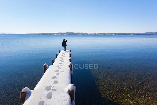 Boy standing on snow covered pier — Stock Photo