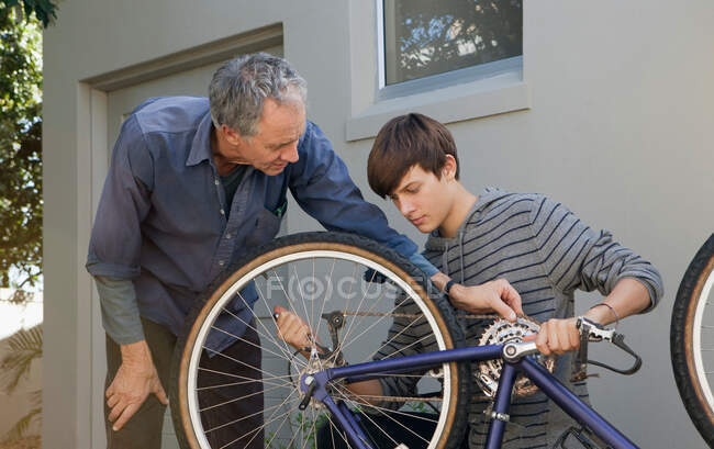 Padre ayudando a su hijo a reparar bicicleta - foto de stock