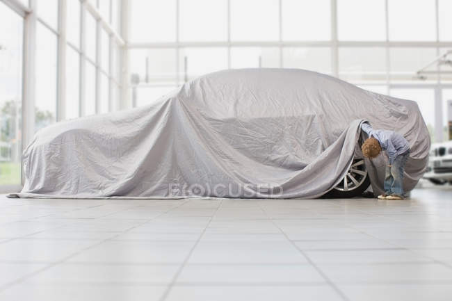 Boy peeking under cloth on car — Stock Photo