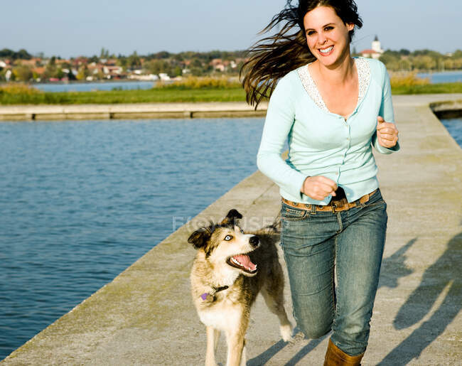 Donna che corre con cane vicino a un lago — Foto stock
