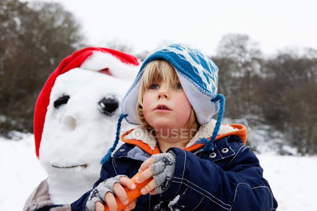 Un chico con una zanahoria para una nariz de muñeco de nieve - foto de stock