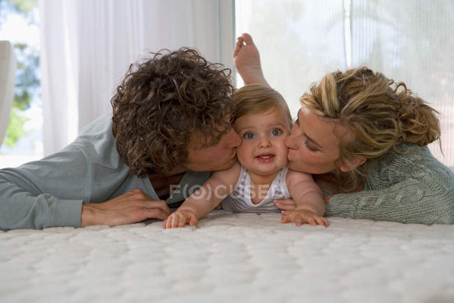 Laying parents kissing baby — Stock Photo