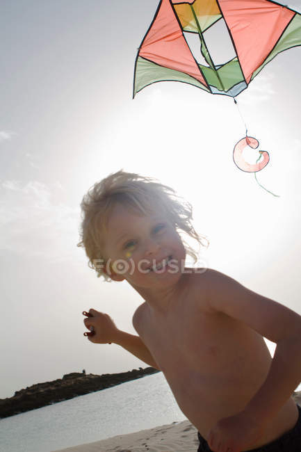Ragazzo sorridente aquilone volante sulla spiaggia — Foto stock