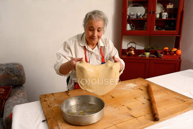 Пожилая женщина растягивает лист теста — стоковое фото
