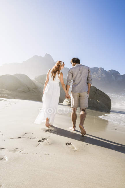 Rückansicht des Paares, das am Strand Händchen haltend geht — Stockfoto