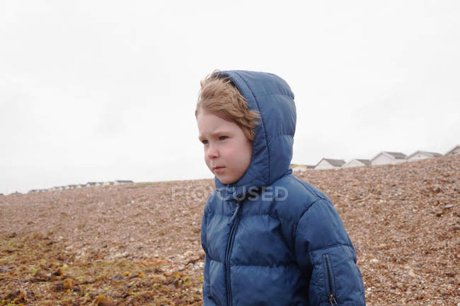 Niño vistiendo parka en la playa rocosa - foto de stock