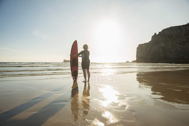 Silhouetted senior woman standing on beach with surfboard, Camaret-sur-mer, Bretaña, Francia - foto de stock