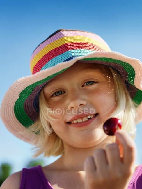 Girl in sunhat holding cherry — Stock Photo