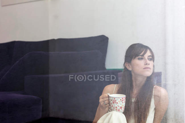 Femme ayant une tasse de café à la fenêtre — Photo de stock