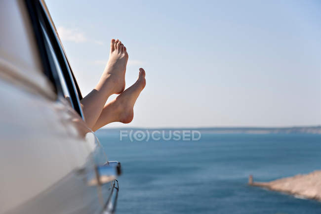 Femme étirant les pieds de la voiture par la mer — Photo de stock