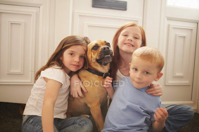 Crianças abraçando cão no chão — Fotografia de Stock
