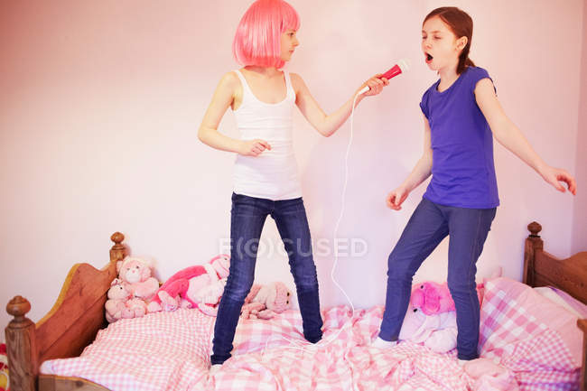 Две девушки, стоящие на кровати и поющие в микрофоне — стоковое фото