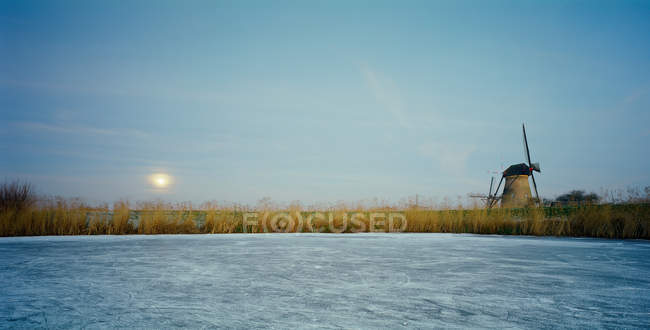 Molino de viento rural en el río congelado por la noche - foto de stock