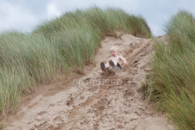 Niño deslizándose por la duna de arena - foto de stock