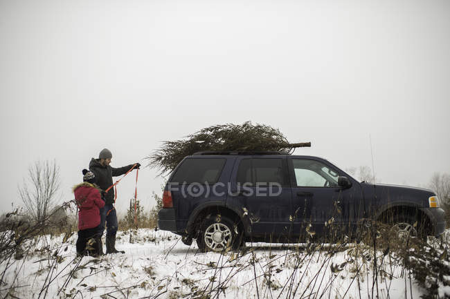Father and daughter tying christmas tree on roof of car — Stock Photo