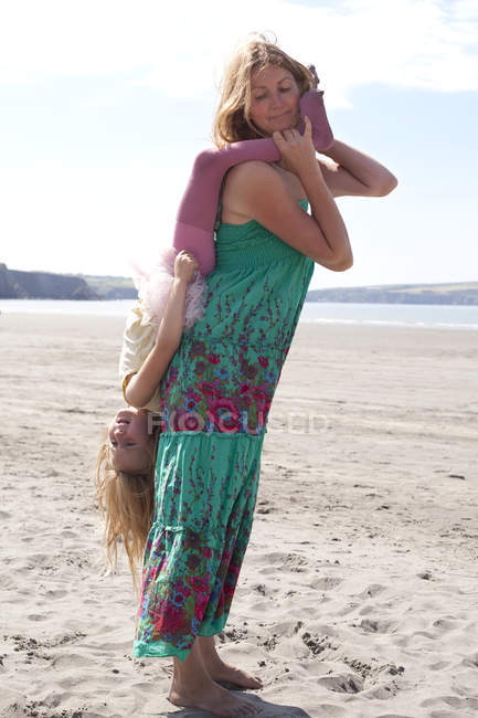 Madre tenendo figlia a testa in giù sulla spiaggia — Foto stock