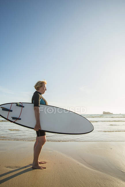 Senior woman standing on beach with surfboard, Camaret-sur-mer, Brittany, France — Stock Photo