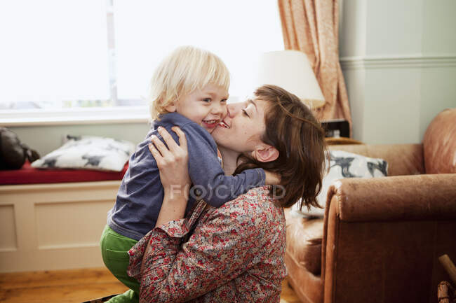 Madre sosteniendo y besando hijo en la sala de estar - foto de stock