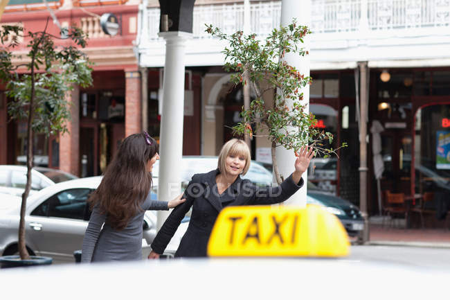 Women hailing taxi cab in city — Stock Photo