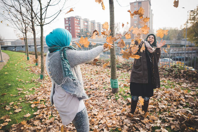 Dos jóvenes juegan peleando con hojas de otoño en el parque - foto de stock