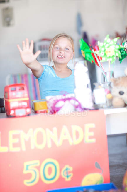 Young girl behind stall with her hand up — Stock Photo