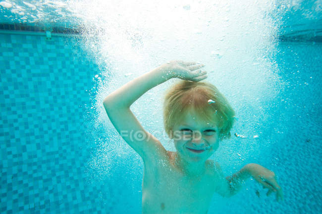 Улыбающийся мальчик плавает в бассейне, избирательный фокус — стоковое фото