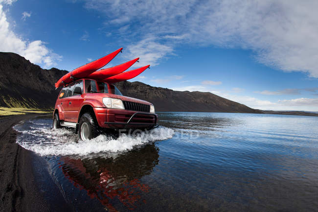 Hombre conduciendo coche en lago poco profundo - foto de stock