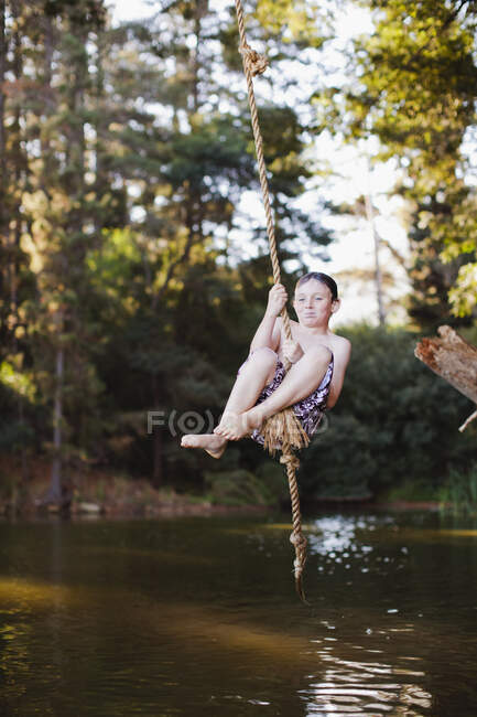 Young boy using rope swing over lake — Stock Photo