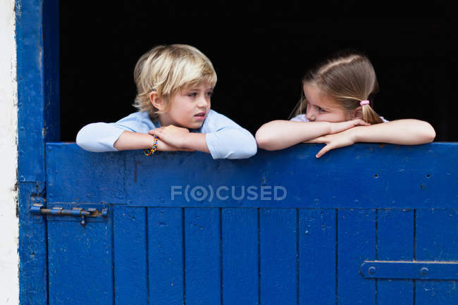 Niños inclinados sobre la puerta azul del granero - foto de stock